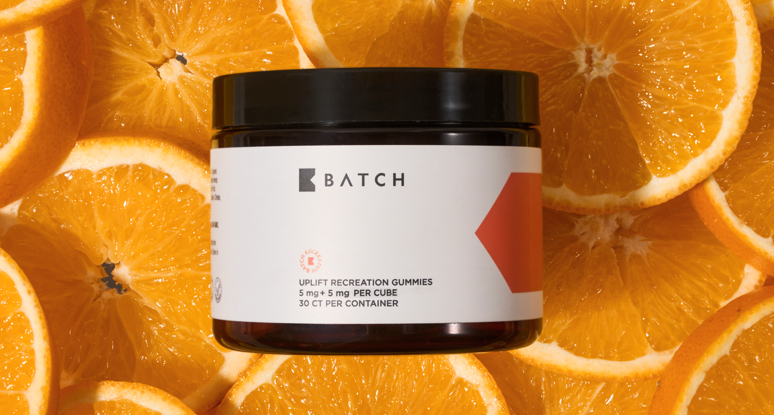 Black jar labeled 'Batch' surrounded by sliced oranges.