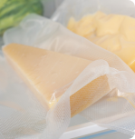 A close-up of cheese wedges wrapped in plastic, on a refrigerator shelf.