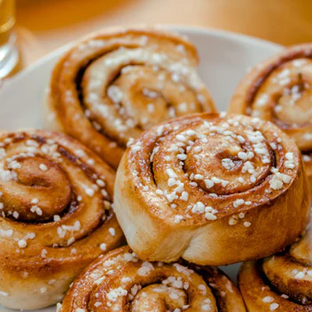 A close-up of several freshly baked cinnamon rolls on a white plate, topped with pearl sugar.