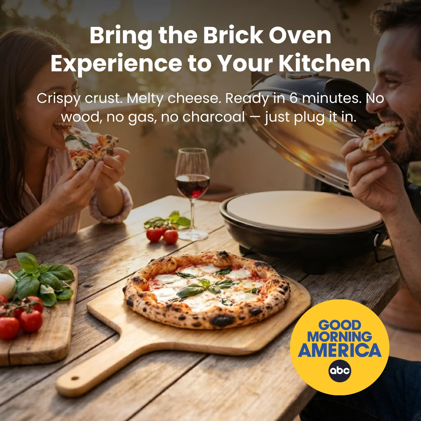 Two people eating pizza at an outdoor table with a portable pizza oven.