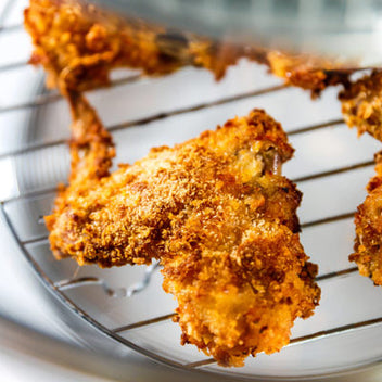 A close-up of a crispy, golden-brown piece of fried food resting on a wire rack.