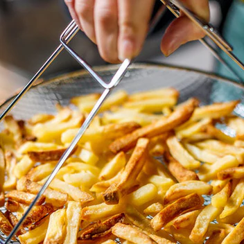 A person lifts a wire basket filled with freshly cooked golden french fries.