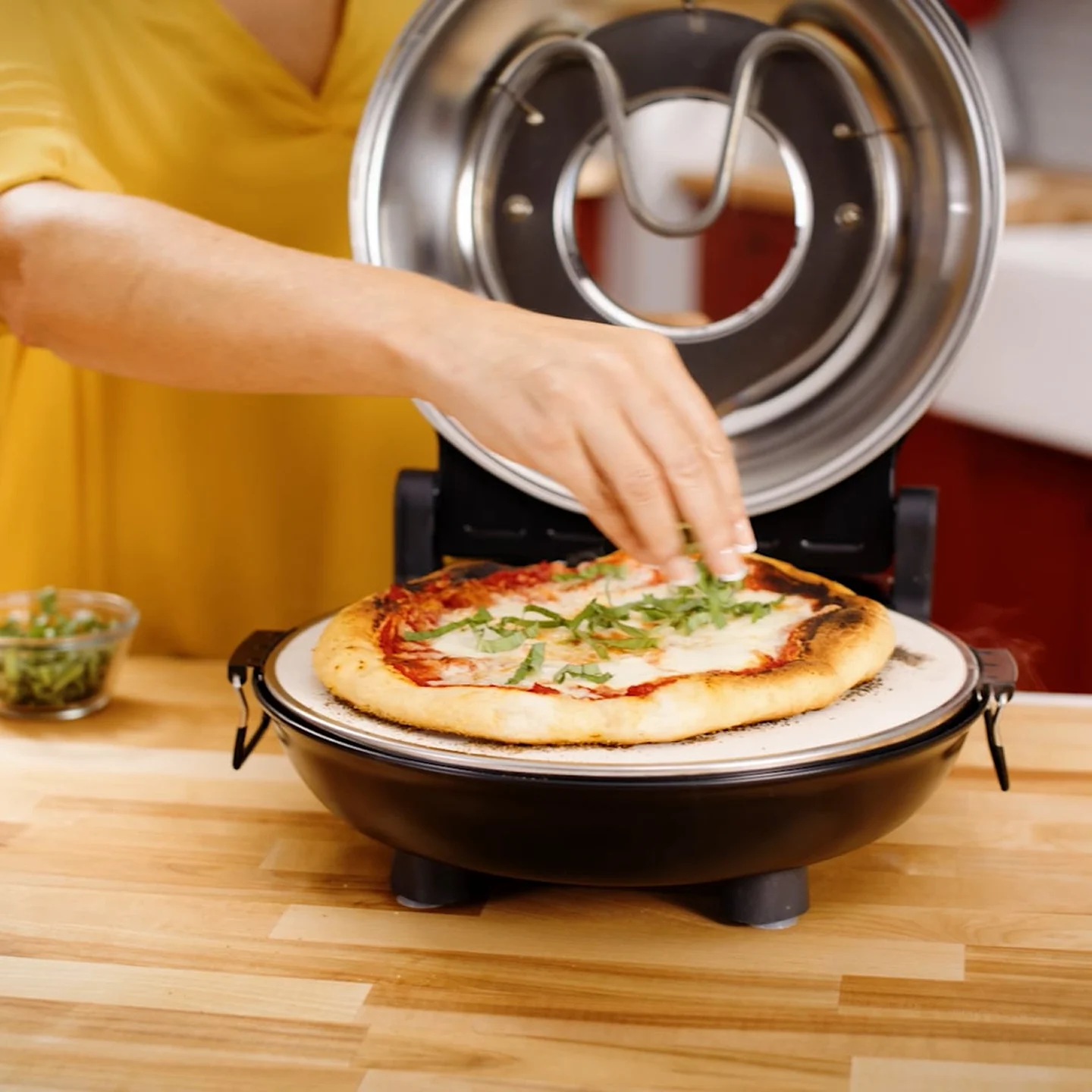 Person adding herbs to a pizza in an open countertop pizza oven.