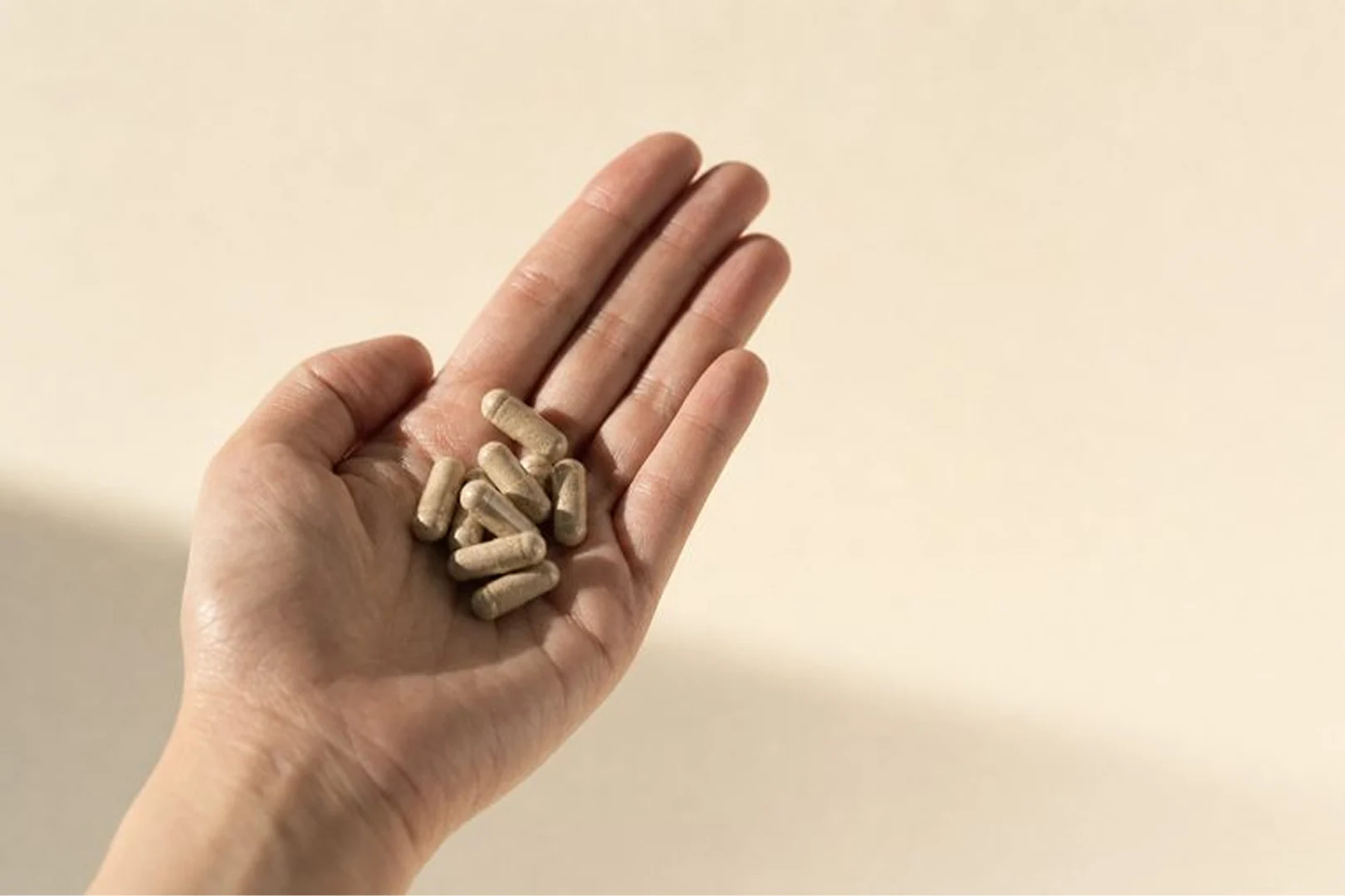 A person's open hand holding a pile of light brown capsules against a plain, off-white background.