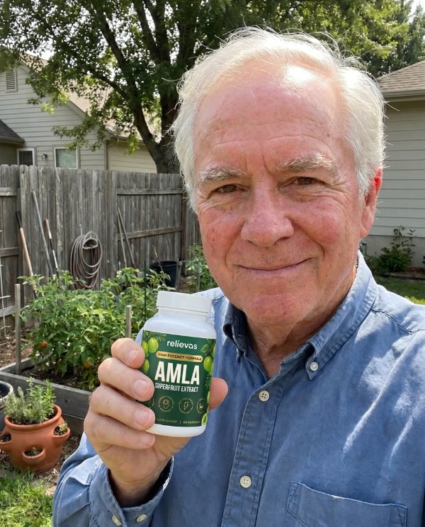 An older man with white hair smiles while holding a bottle of Amla supplements in a backyard garden.