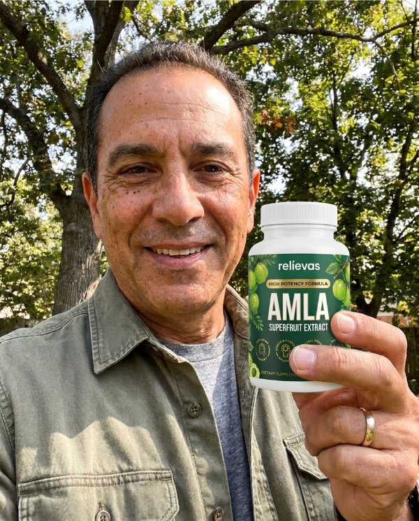 A smiling man stands outdoors holding a white bottle of Relievas Amla Superfruit Extract supplements.