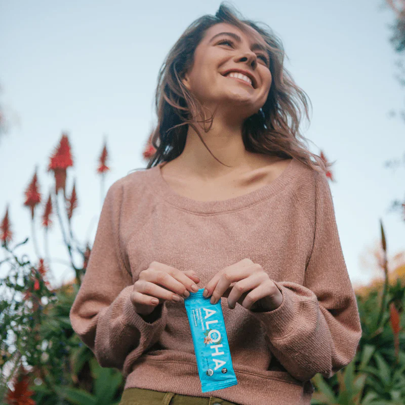 Smiling person holding an ALOHA bar in a garden setting.