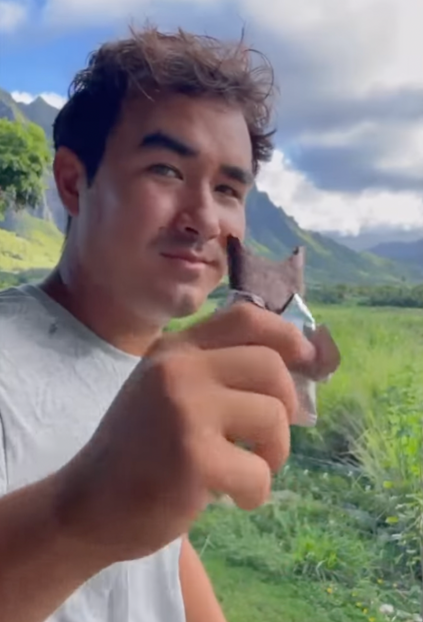 Man holding a piece of chocolate with a scenic mountain view in the background.
