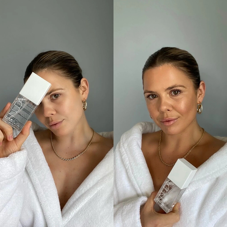 Person in a white robe holding a skincare product bottle.
