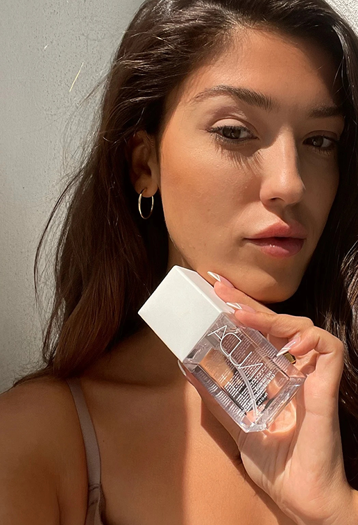 Person holding a clear bottle with a white cap against a plain background.