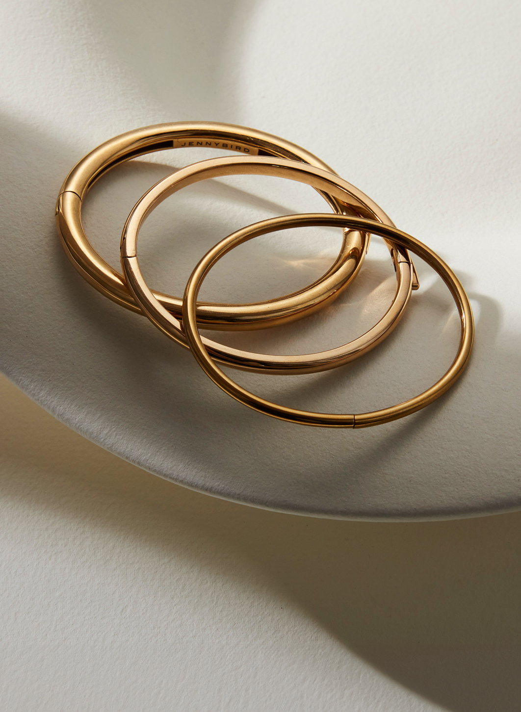 Three gold bangles on a soft, light surface.