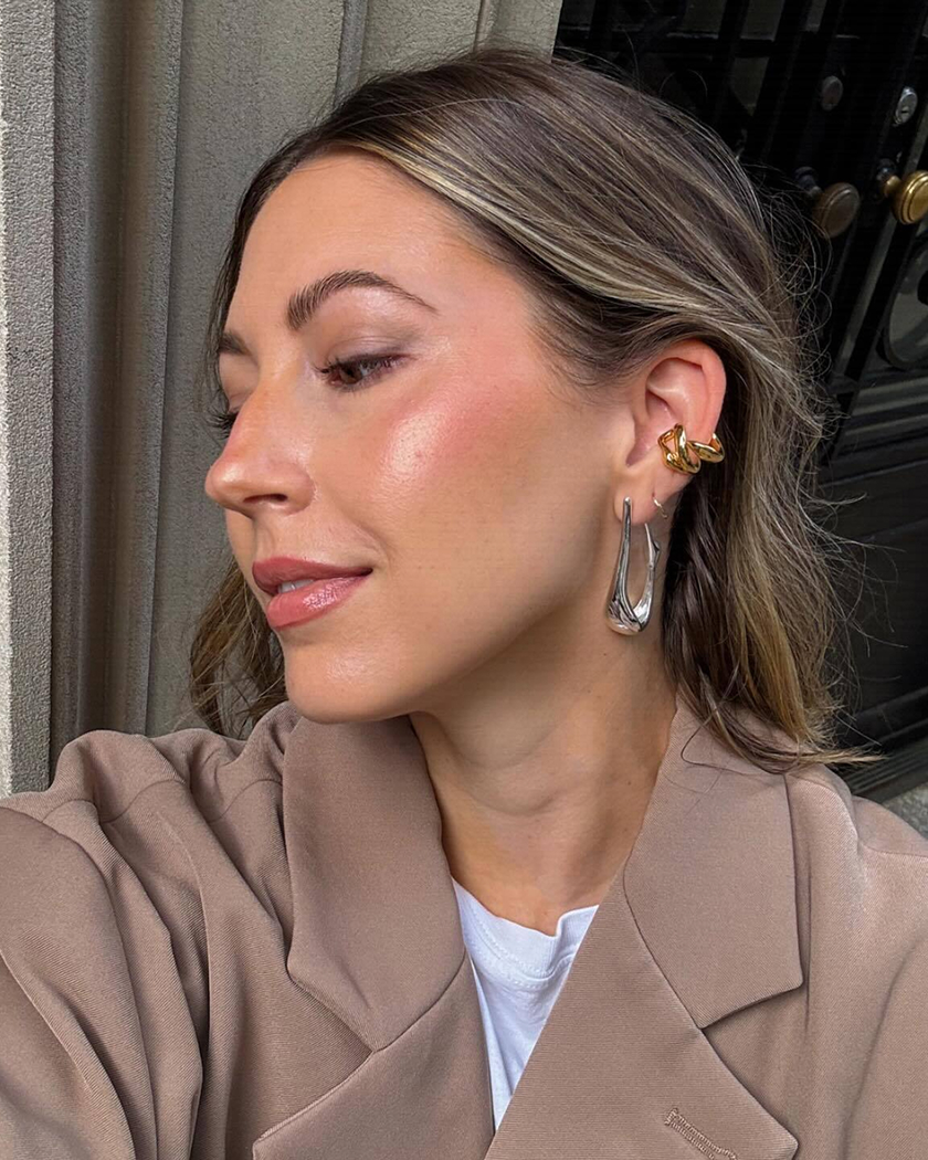 A woman with hoop earrings and a brown jacket, facing sideways.