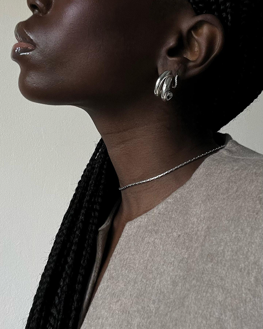 Person wearing silver earrings and necklace, with braided hair and neutral-toned clothing.