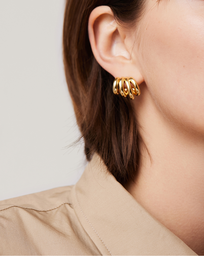 A close-up of a person's ear showing a multi-layered gold hoop earring and a tan collared shirt.