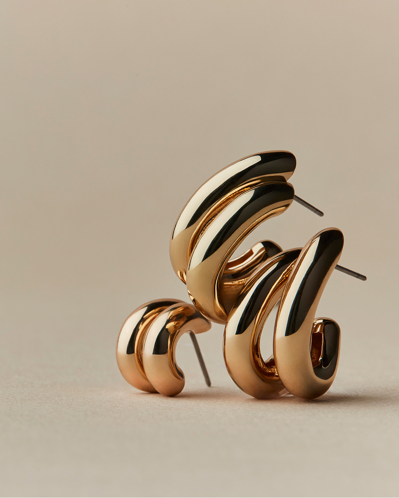 A pair of sculptural, gold-toned hoop earrings in two sizes against a neutral background.