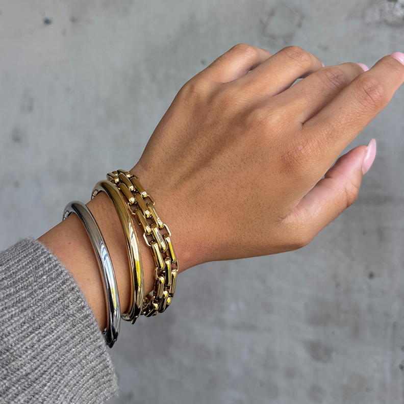 A hand wearing three different metallic bracelets against a gray background.