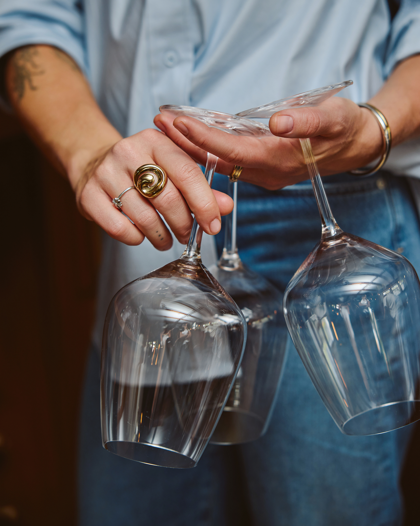 A close-up of a person's hands holding several empty wine glasses by their bases.