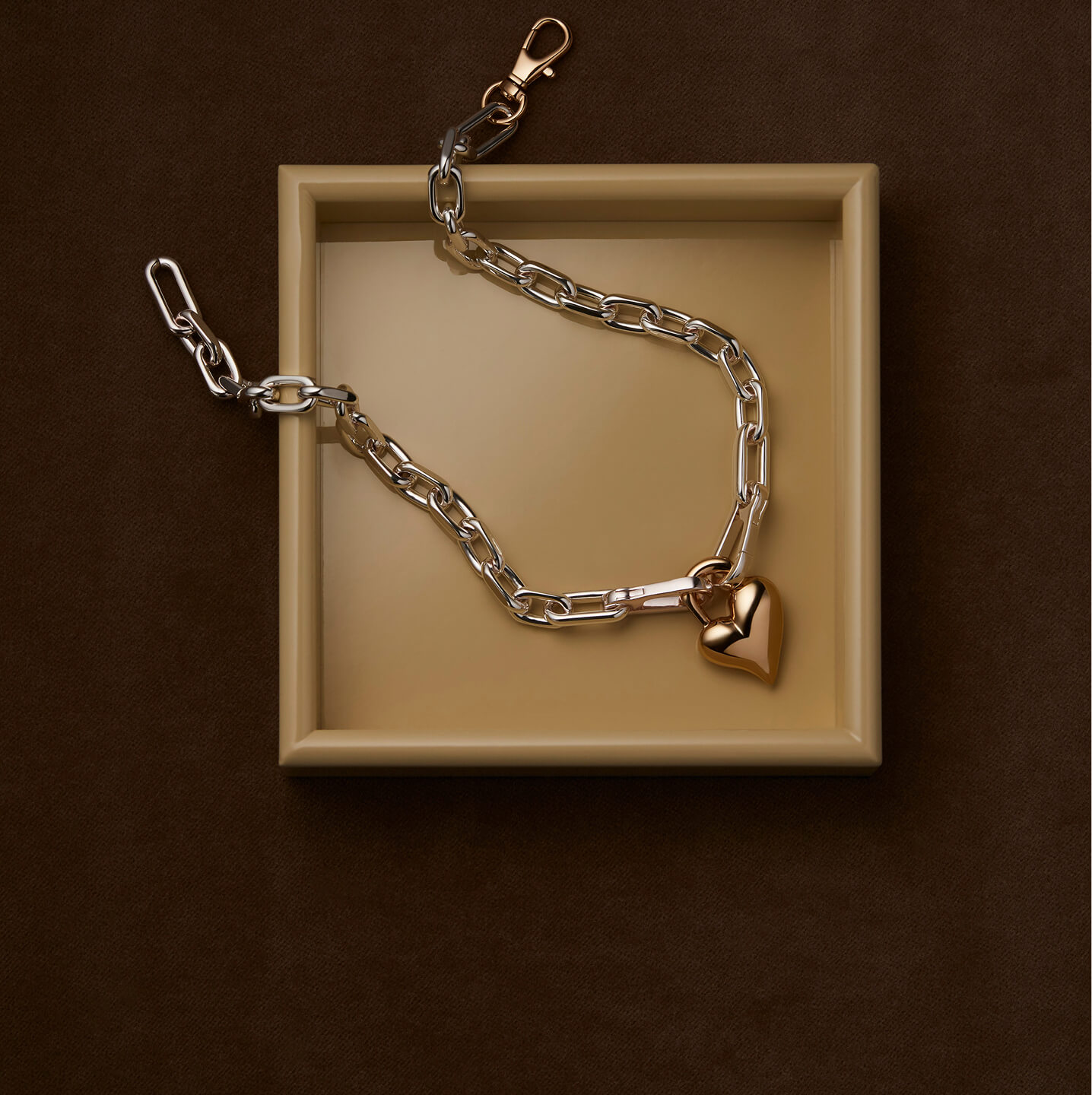 Silver chain with a gold heart pendant on a beige tray.