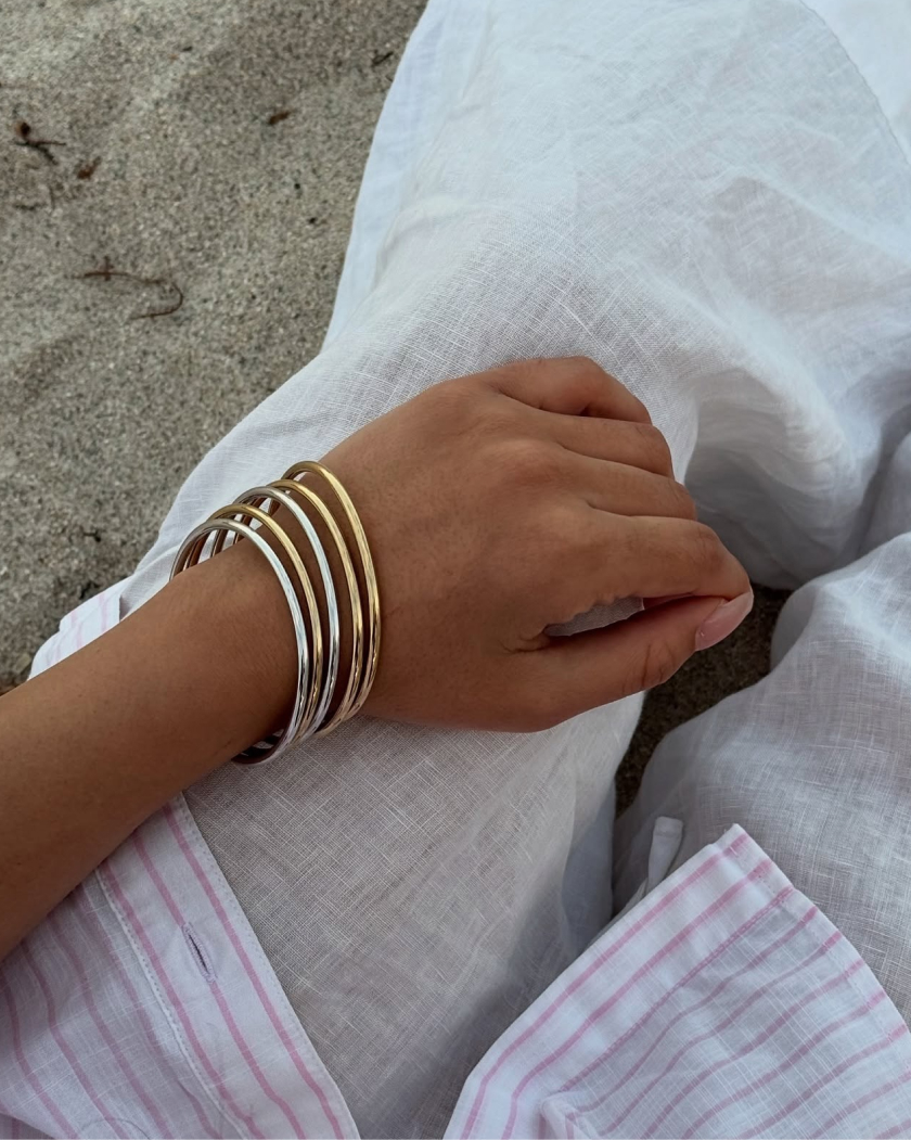 Hand with gold and silver bangles on white fabric background.