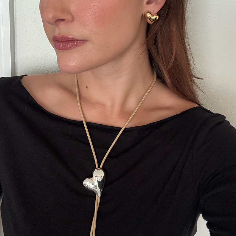 Person wearing heart-shaped necklace and earring.