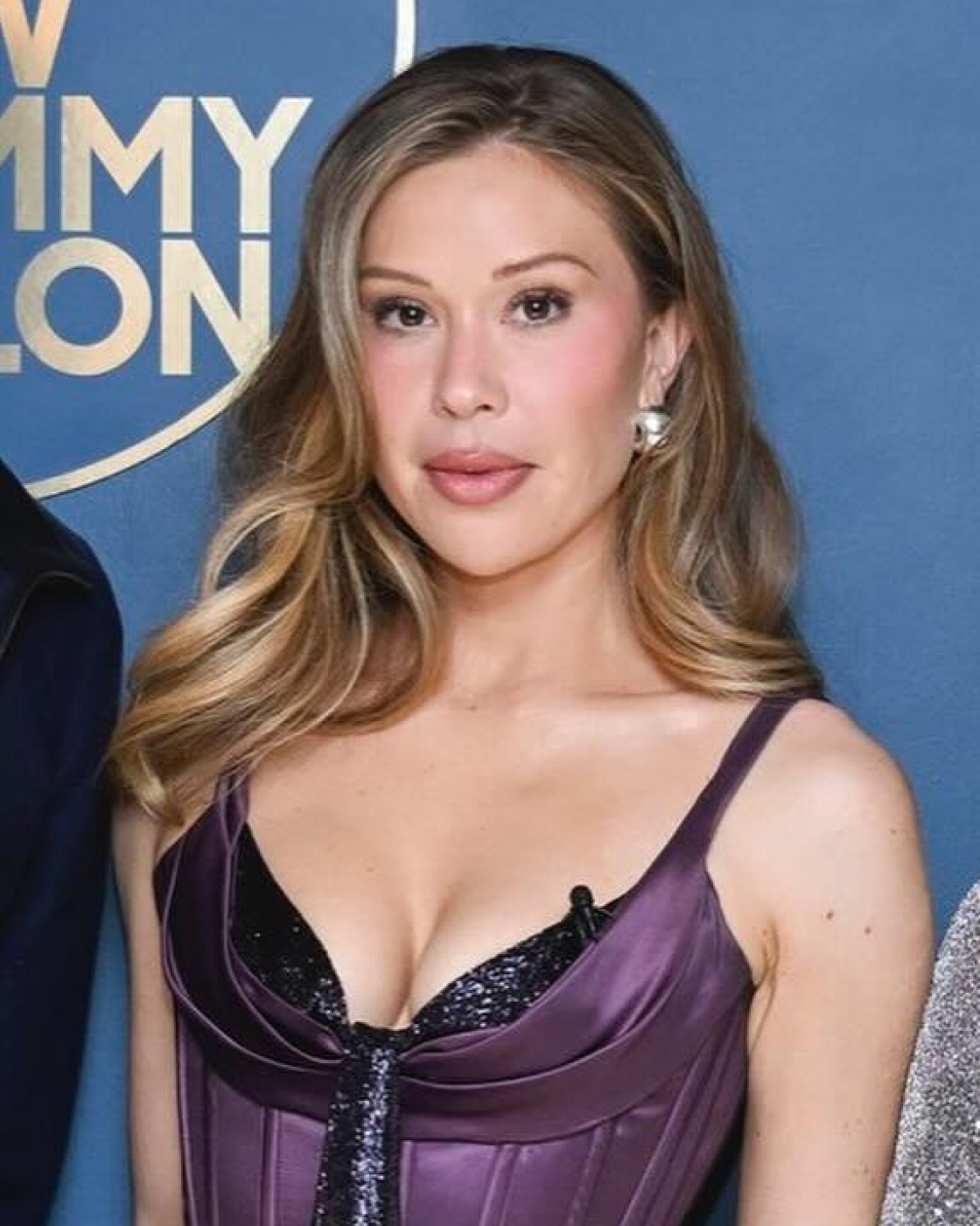 A woman in a purple dress stands in front of a blue background.