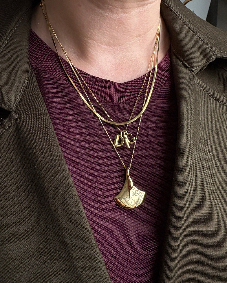 A close-up of a person's neck wearing a burgundy sweater, green jacket, and several layered gold necklaces.