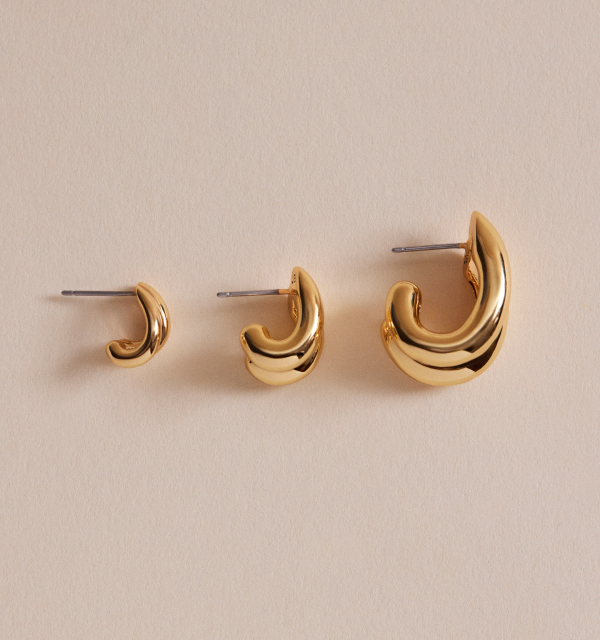 Three gold hoop earrings of increasing size on a beige background.