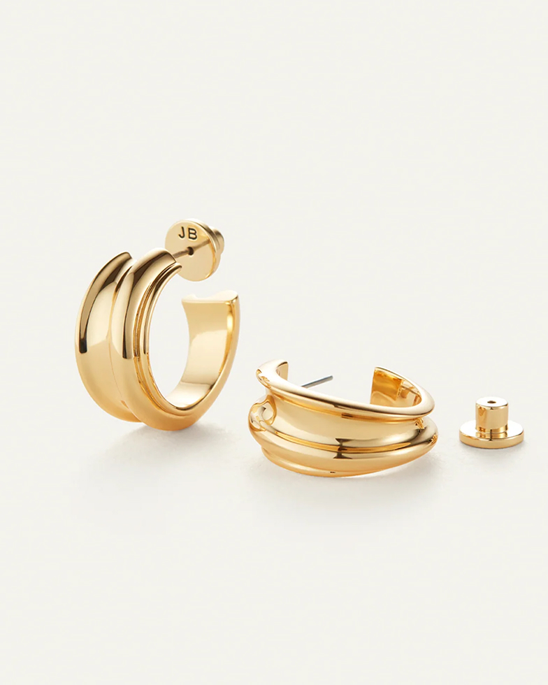 A pair of shiny, gold, double-ridged C-hoop earrings with post backs on a plain off-white background.