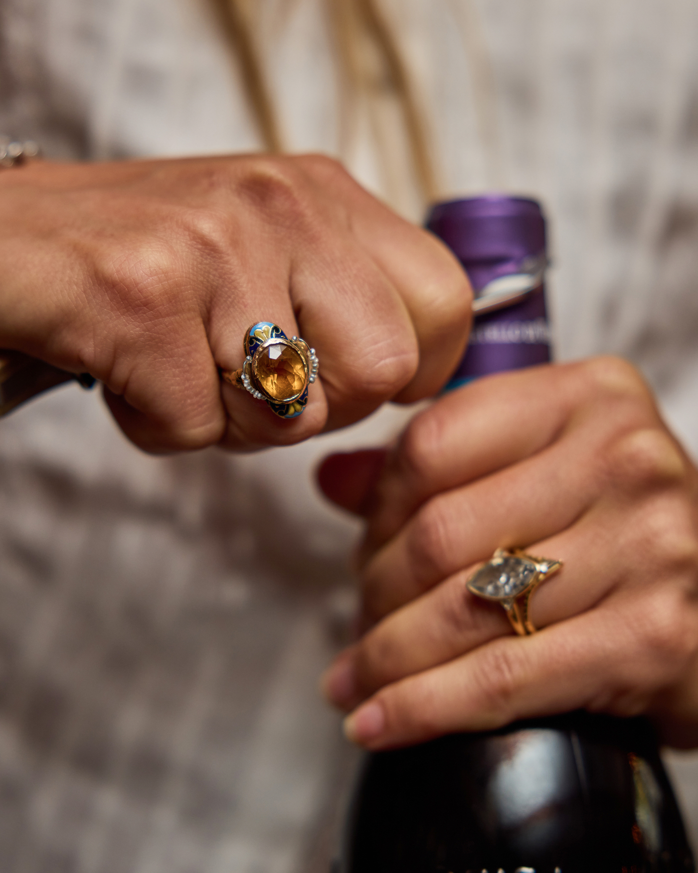 A close-up of a person's hands wearing ornate rings while opening a bottle of wine.