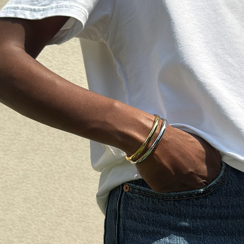Person wearing bangles and a white t-shirt with hand in denim pocket.