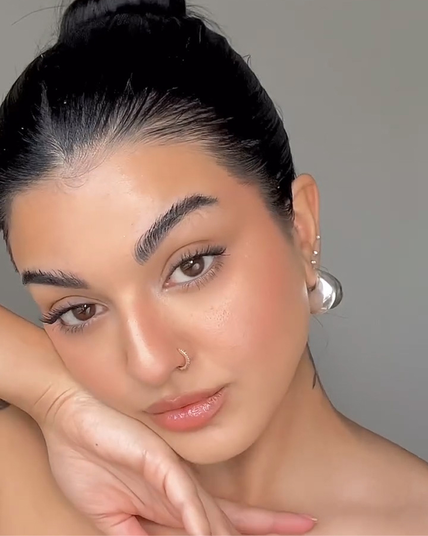 Woman with dark hair and nose ring, resting her face on her hand.