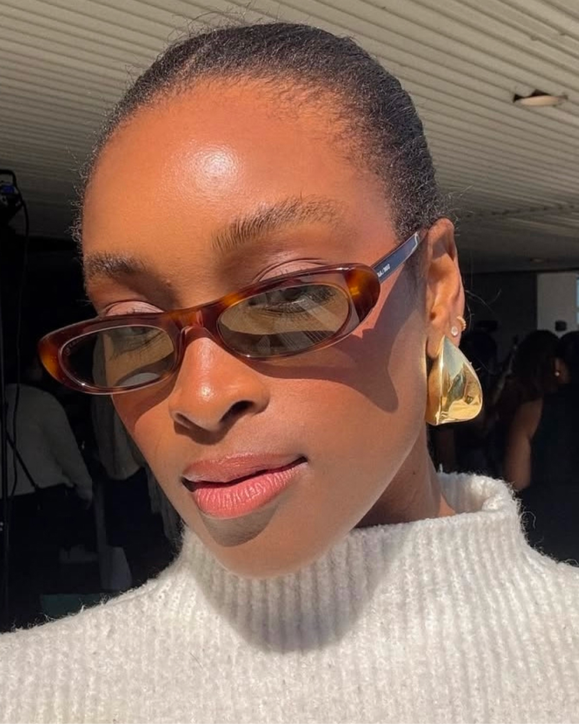 Person wearing sunglasses and a white sweater, basking in sunlight indoors.