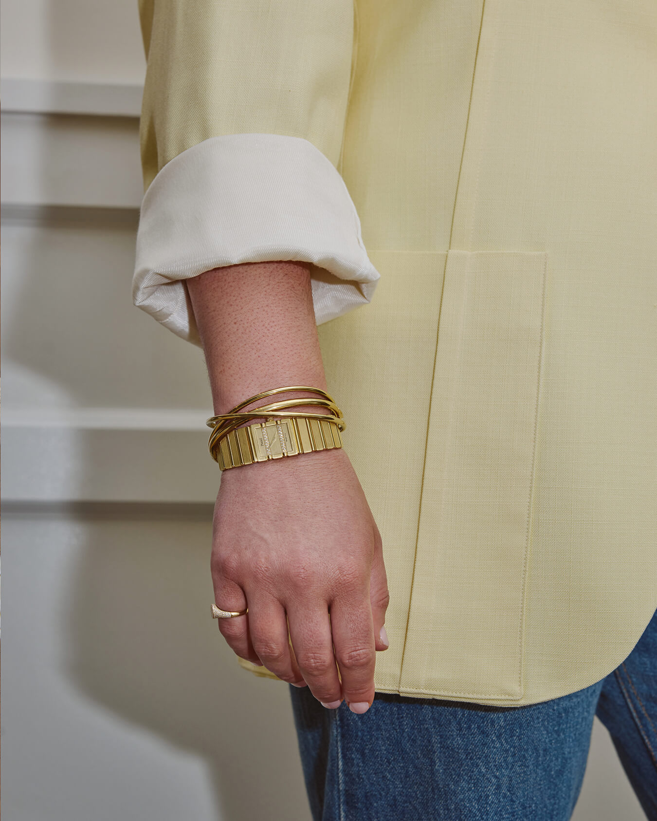 A close-up of a person's wrist wearing gold bracelets and a ring, with a yellow blazer sleeve.