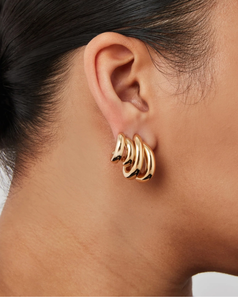 A close-up of a person's ear wearing a chunky, gold, triple-hoop earring.