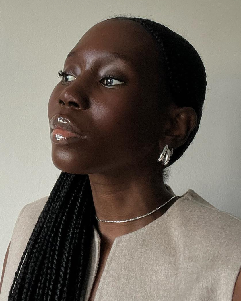 Person with braided hair, wearing earrings and a necklace, looking to the side.
