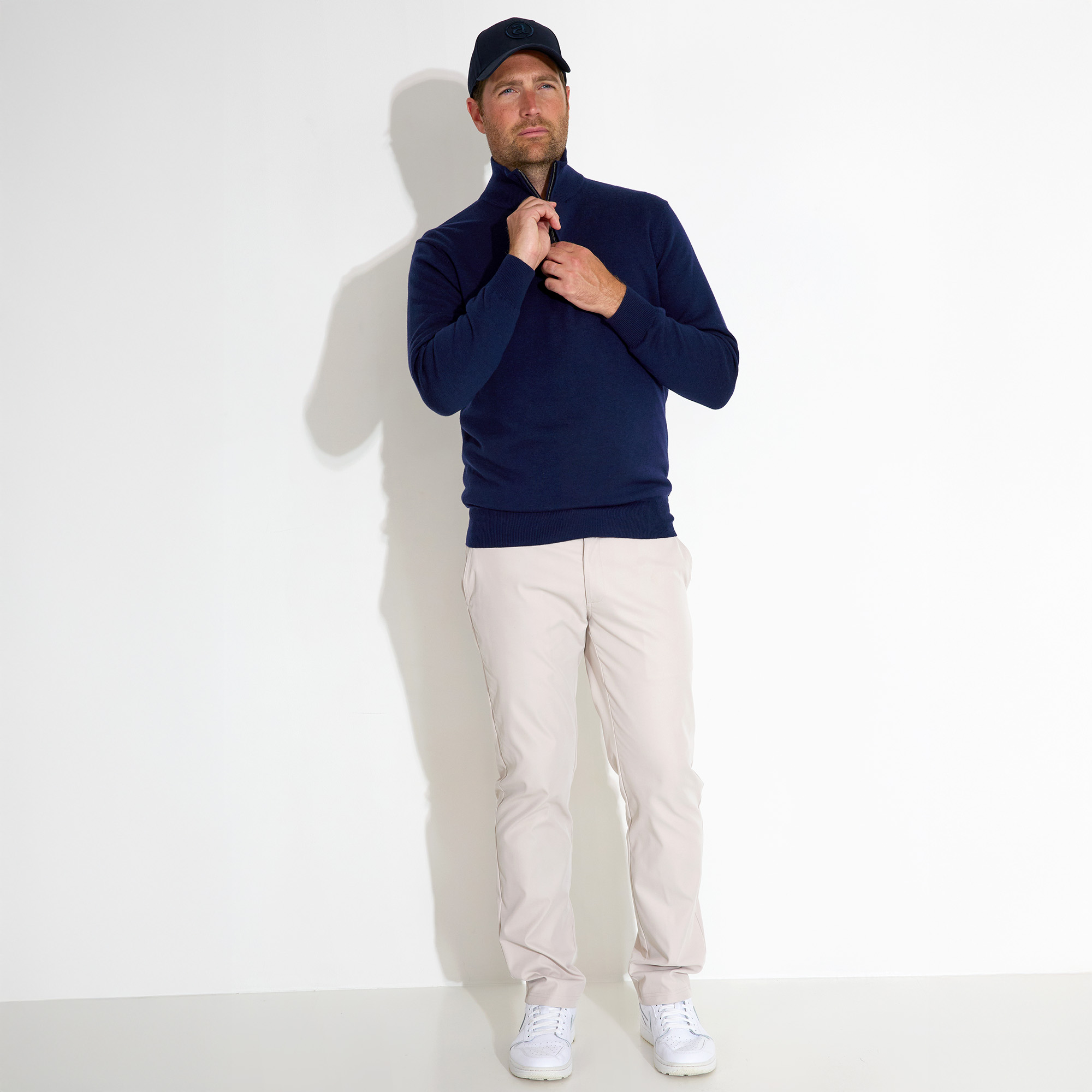 Man in navy sweater and cap, standing against a white background.