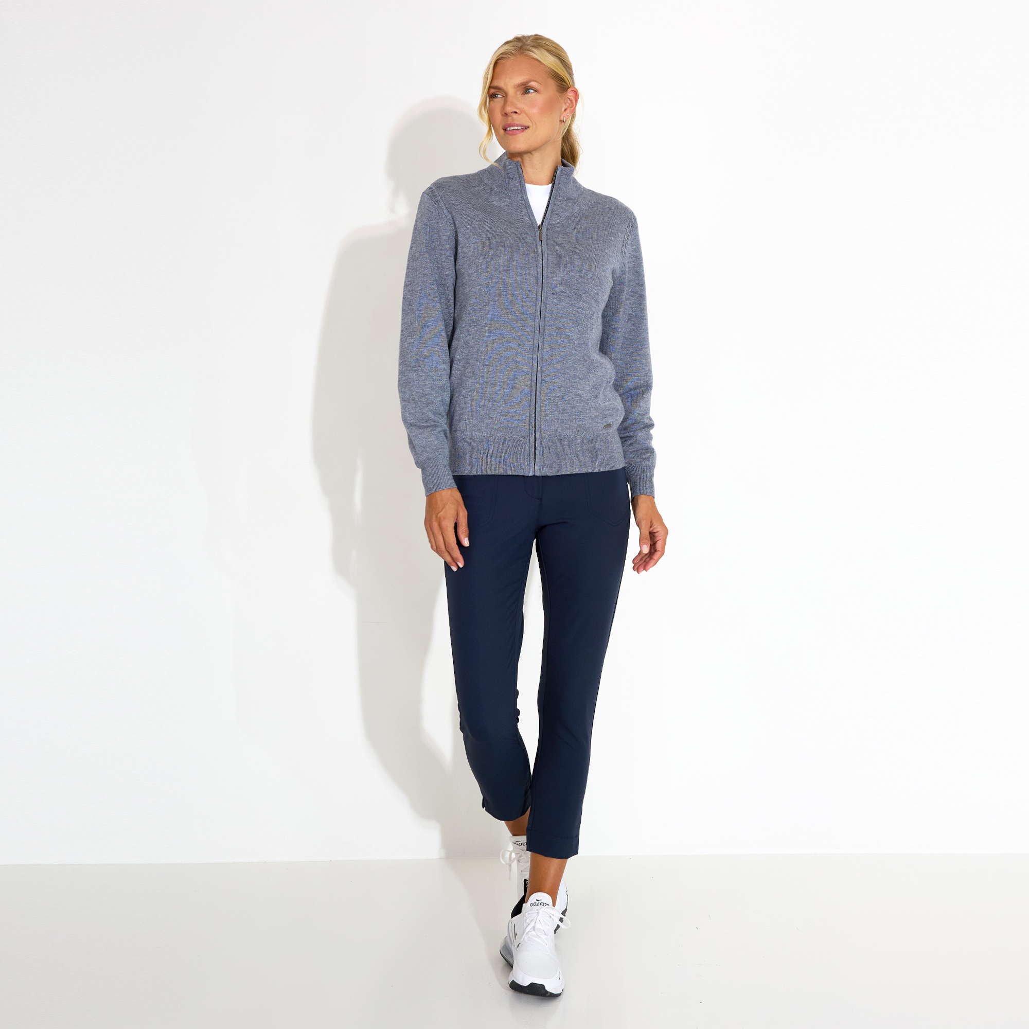 Person wearing a gray zip-up sweater and navy pants against a plain background.