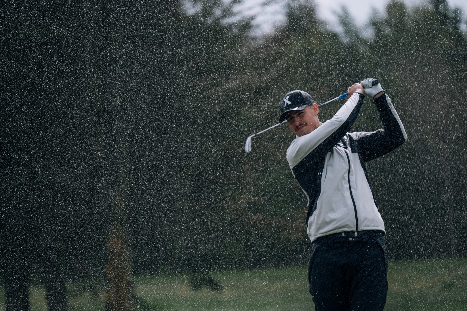 Golfer swinging a club in the rain on a golf course.