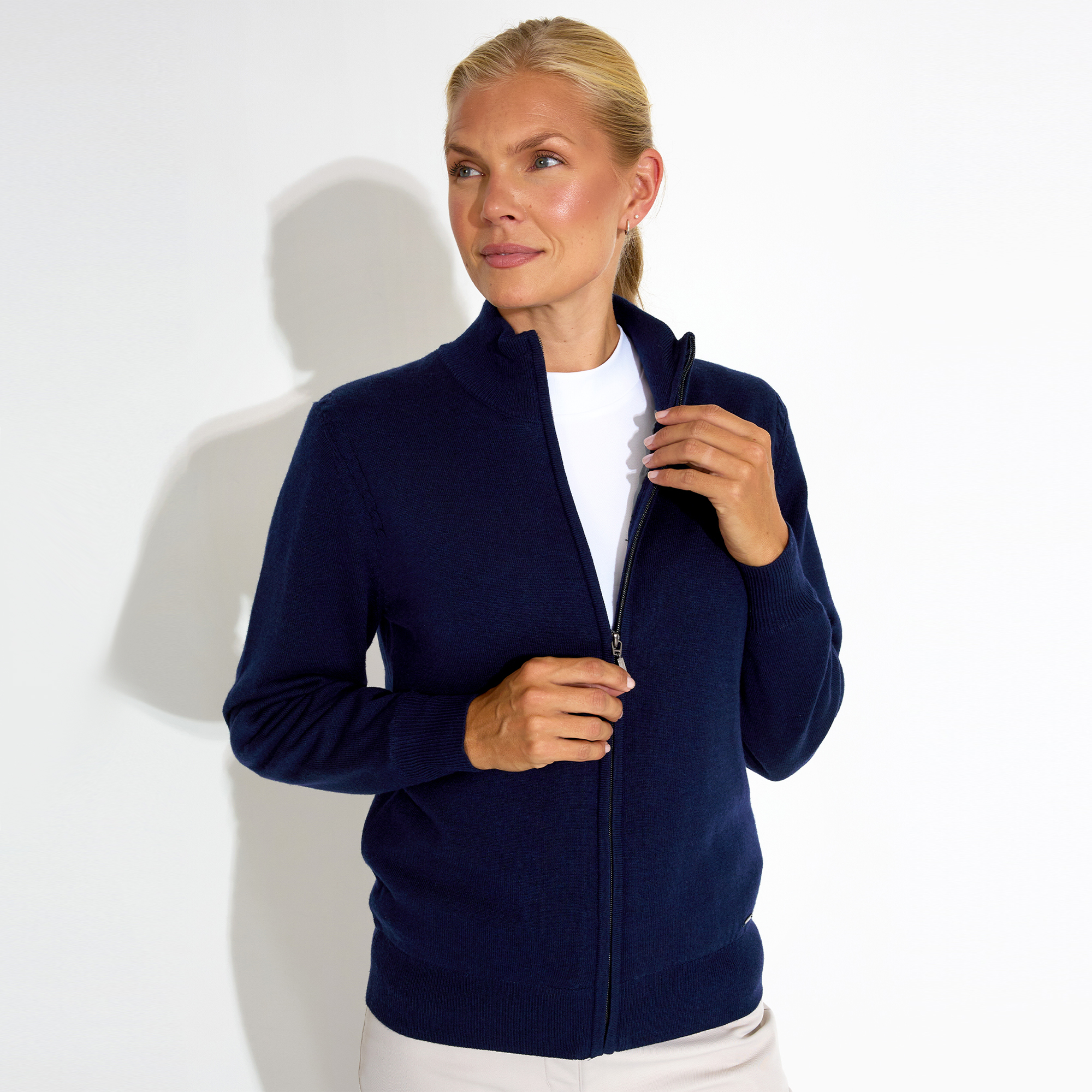 Person wearing a navy zip-up sweater and white shirt against a plain background.