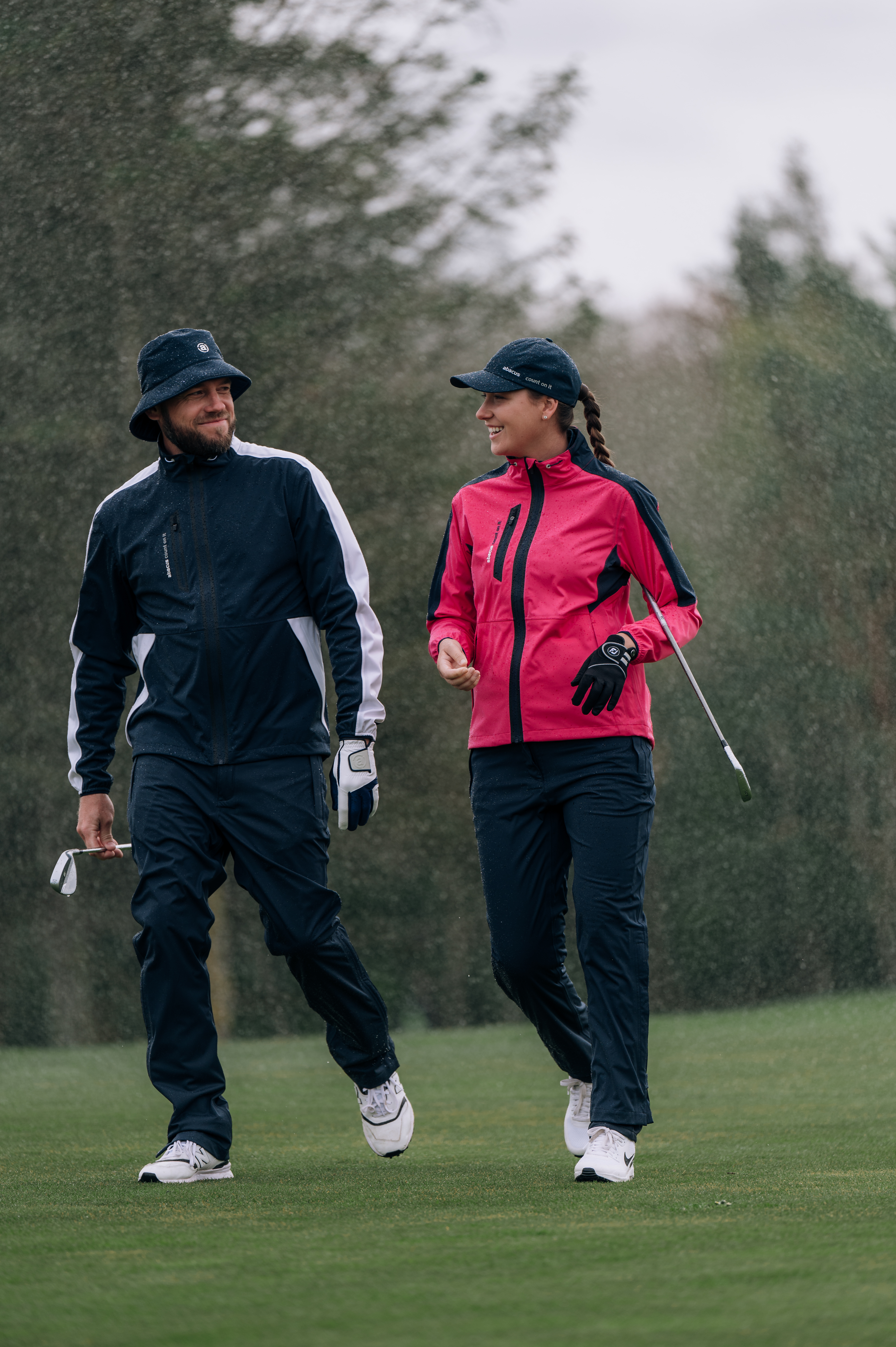 Two people in rain gear walking on a golf course.