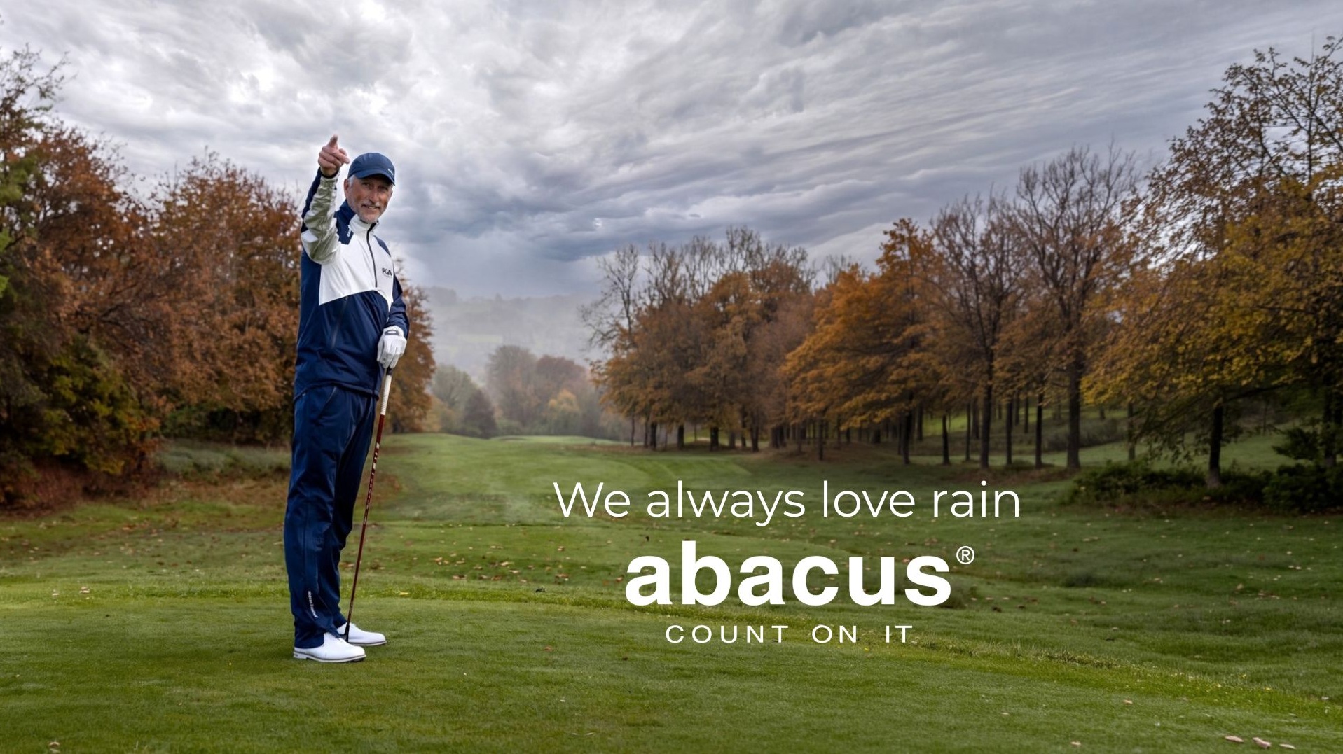 A smiling male golfer points up at a cloudy sky on a golf course in autumn.
