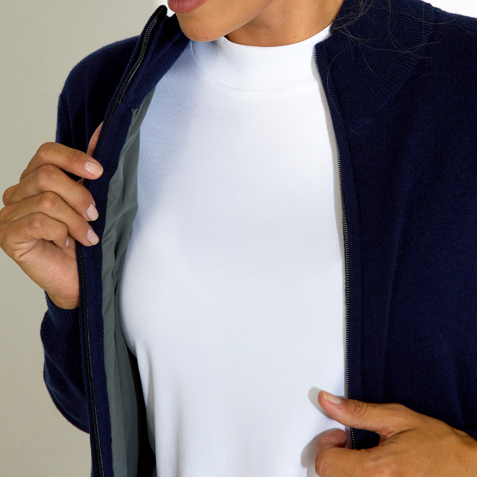 Person wearing a blue jacket over a white top, partially unzipping.