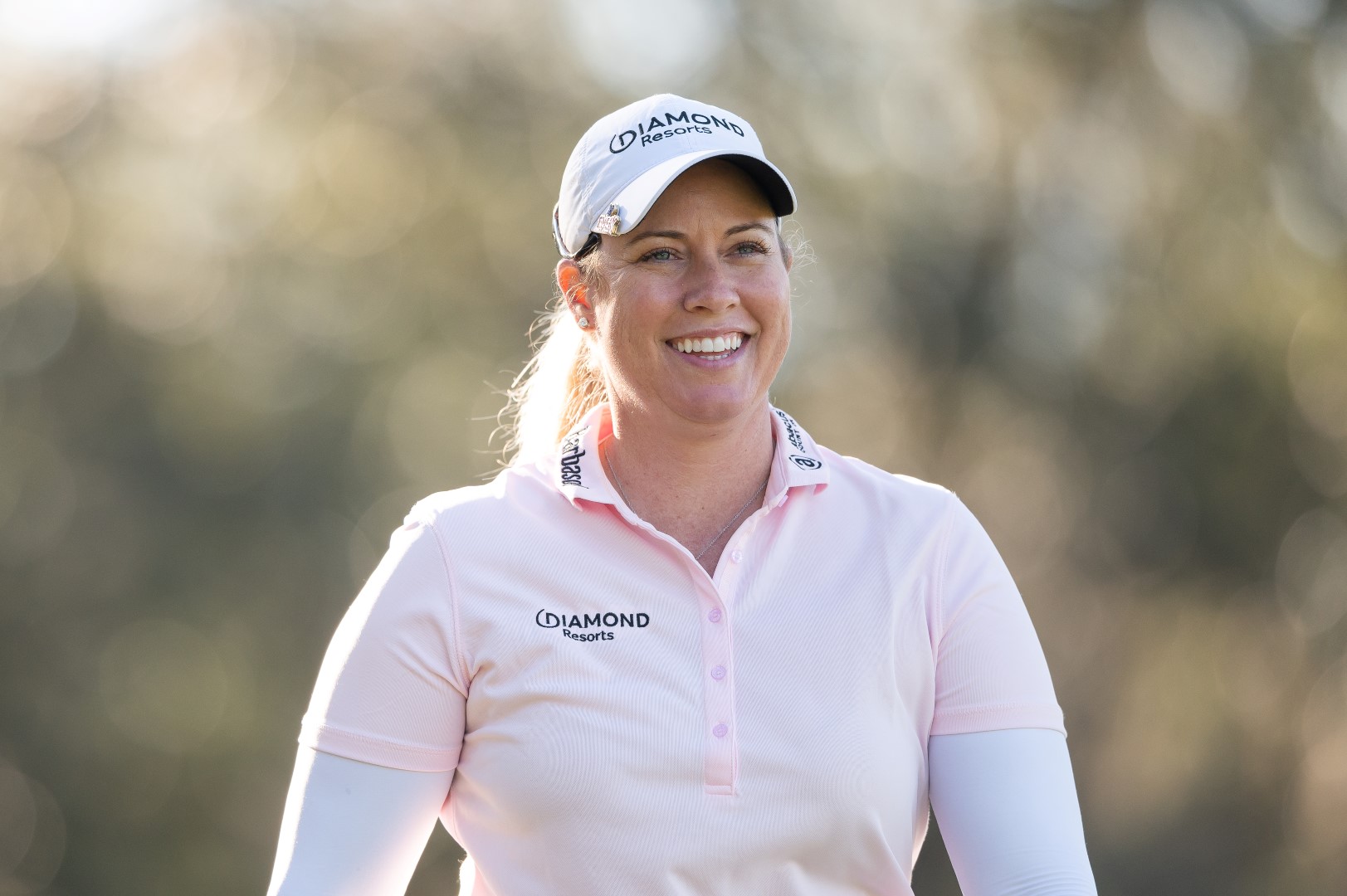 Person in a pink shirt and cap smiling outdoors.