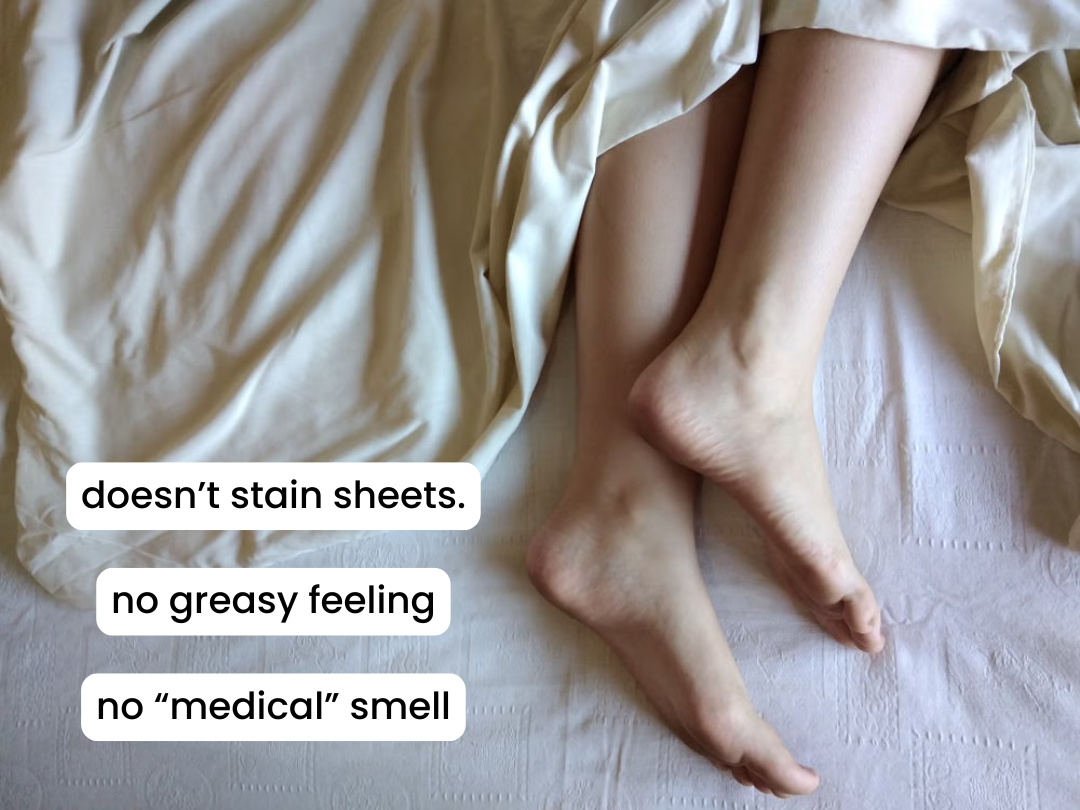 A person's bare legs and feet resting on a bed with rumpled white sheets.