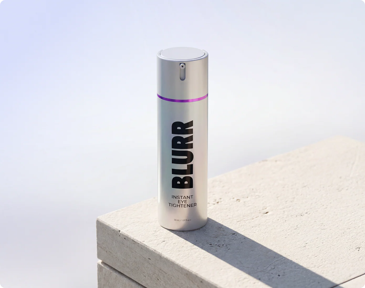 A silver bottle of Blurr Instant Eye Tightener resting on a stone surface against a light background.