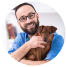 Man in blue shirt holding a small brown dog, smiling.