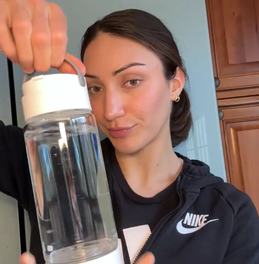 Hand holding a clear water bottle with a black cap and logo.