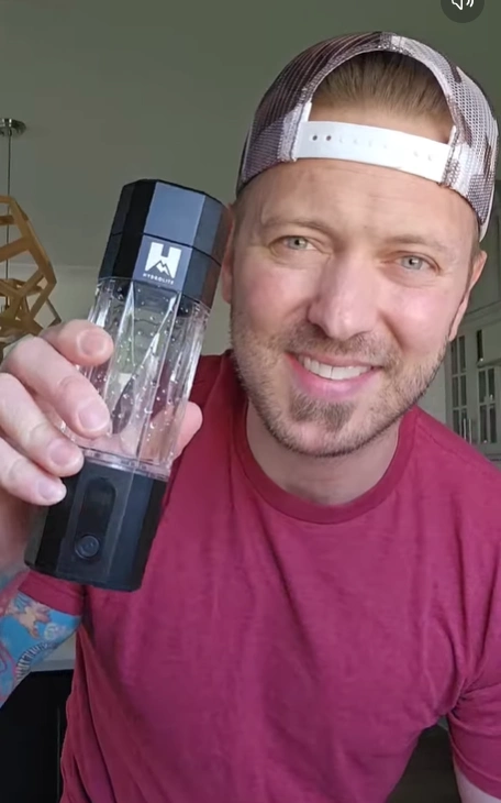 Person holding a black and clear portable blender, smiling.