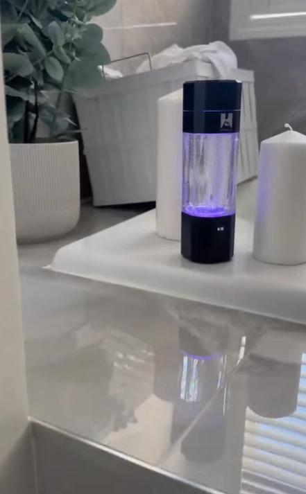 A countertop with a glowing bottle, candles, and a plant in a bathroom setting.