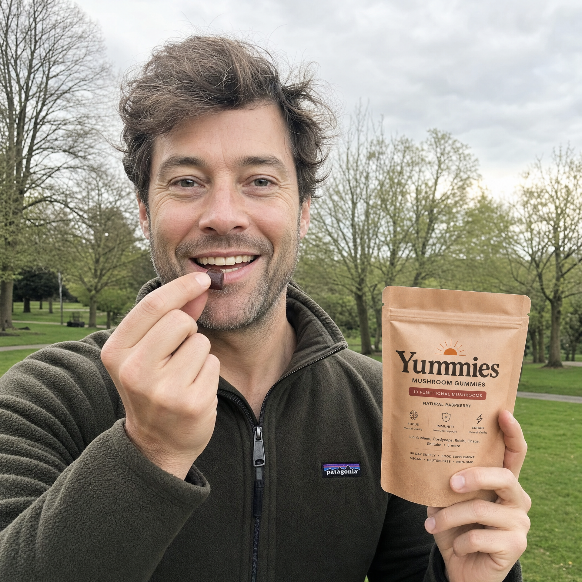 A man in a park smiles while eating a Yummies mushroom gummy and holding the pouch.